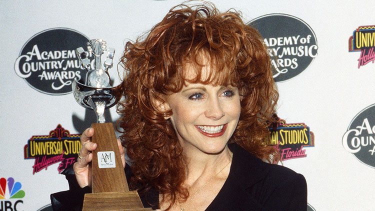 Reba McEntire with red hair smiling and holding her Academy of Country Music Award.